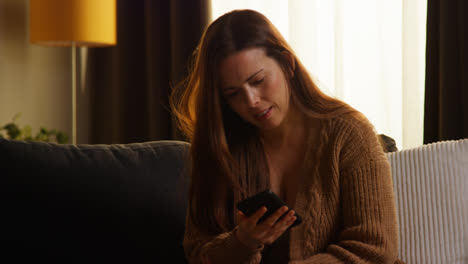 Shocked-Woman-Sitting-On-Sofa-At-Home-Using-Mobile-Phone-To-Check-Social-Media-Message-And-Scrolling-Online-1